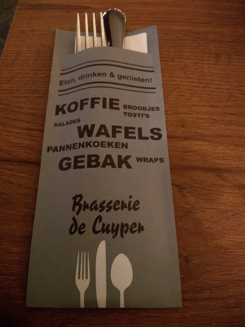 Het grijsblauwe bestekzakje van Brasserie de Cuyper met de kaart: koffie, broodjes, tosti's, salades, wafels, pannenkoeken, gebak en wraps