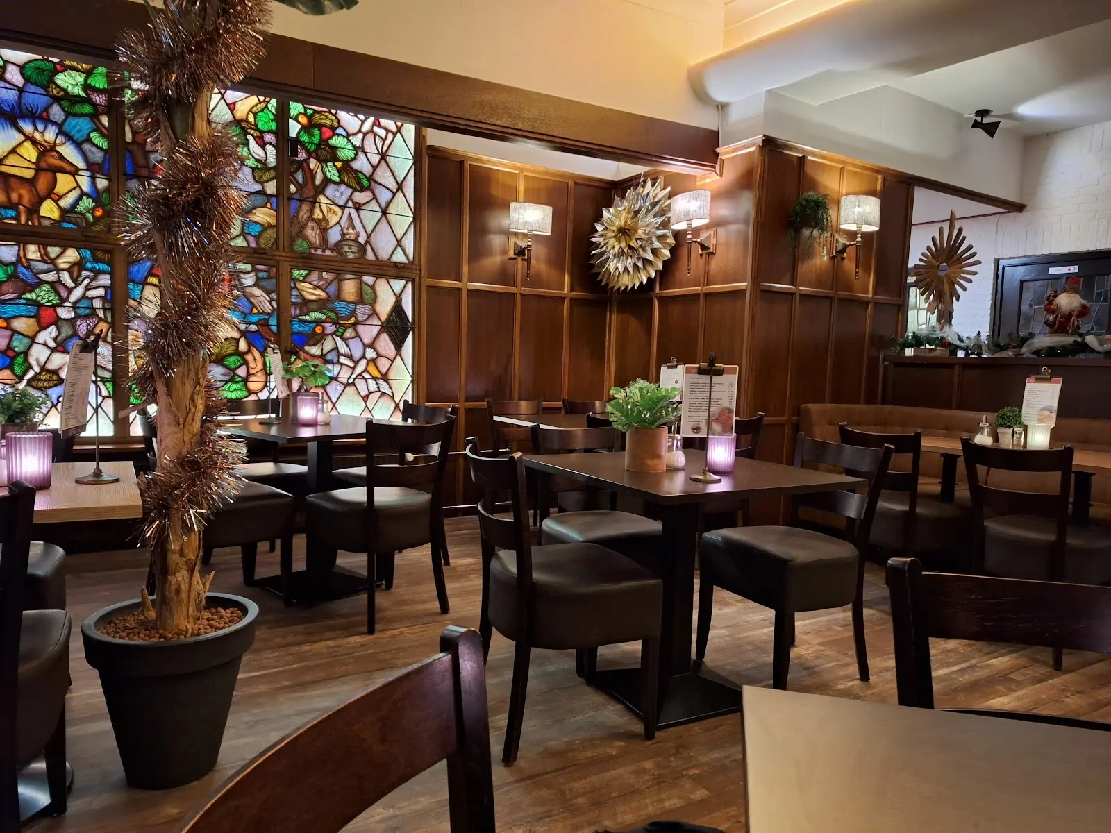 Het interieur van Brasserie de Cuyper: glas-in-loodramen, houten lambrisering en tafels met kaarsjes